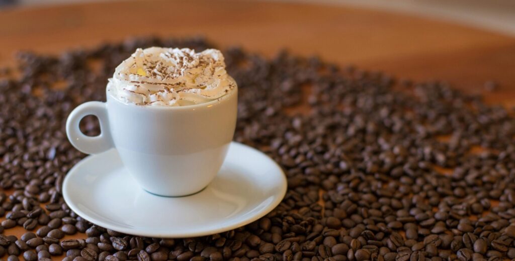 Delight in a creamy coffee topped with whipped cream, nestled among roasted coffee beans.